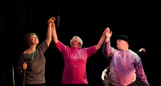 3 people standing in a line, holding hands raised in the air and looking upwards. 