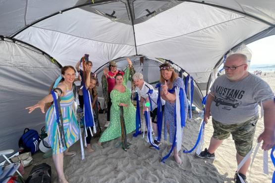 colurful dancers with blue and white ribbons on their wrists standing in a silver tent on the beach