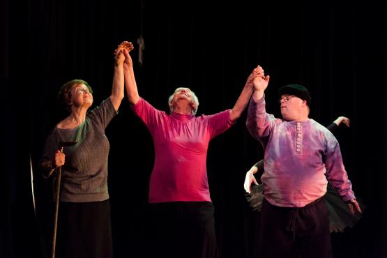 3 people standing in a line holding hands raised upwards.