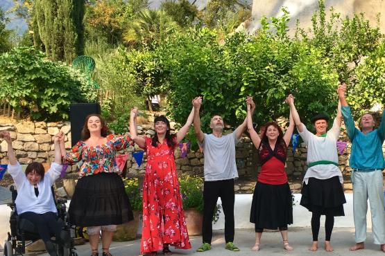 A group of seven dancers preparing to take a bow at the end of a performance. They have joined hands and all have their hands in the air. The group includes a dancer in a wheelchair and six dancers standing.