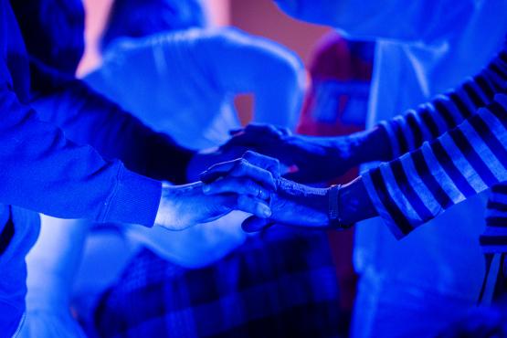 2 pairs of hands are meeting in the middle, bathed in a blue background where we can see the outlines of other people dancing