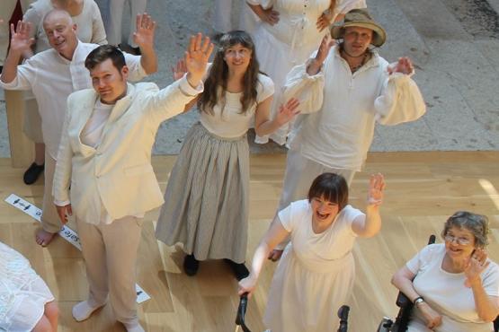 People are waving up at the camera from far below in white costumes