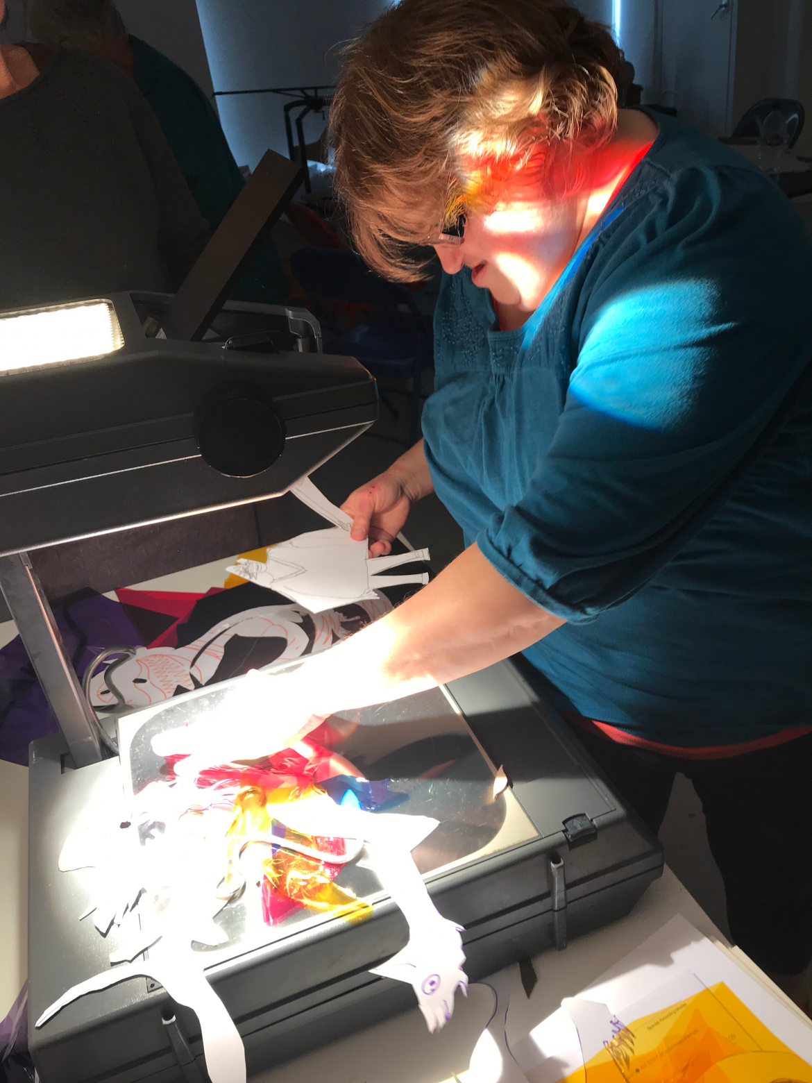 A person in a blue top laying out cut outs onto an overhead projector