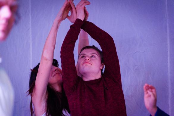 2 people dancing. They are standing close together and are both reaching their hands above their heads and looking upwards
