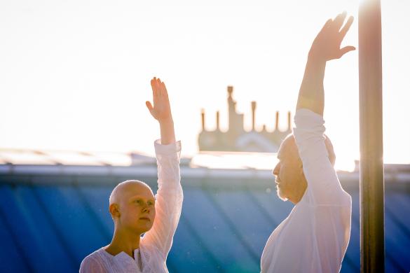 2 people in white upper bodies with one raised arm blue lower background light abov
