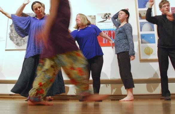 Four people dancing in a light-filled art gallery with paintings on the wall behind them