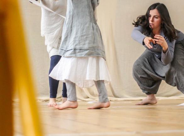 Three people dancing in a room lit with natural light against a white backdrop. One is crouching down, the others are upright.