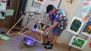 a person playing a homemade instrument which is made out of wood on the floor. The person is bent over hitting it with a stick. 