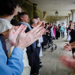 Many performers are cheering and clapping at the end of the show. They are outside under large pillars.