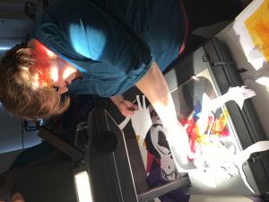 A person playing with paper cutouts on an overhead projector plate to create images on the wall 