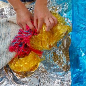 a pair of hands playing with yellow, blue, pink and silver textile materials