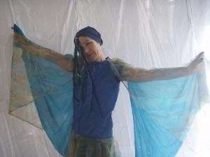 A person dressed up in a blue costume. The costume has blue long wings and a blue turban. The person is holding their arms out to show the blue long wings. 