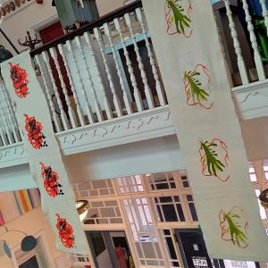 Banners hanging from a balcony in a big public space. The banners have colourful prints on them inspired by seaweed.