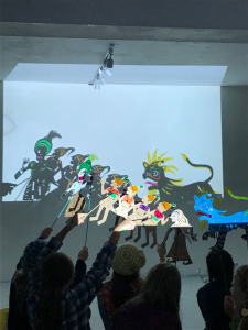 Young people holding up their shadow puppets in front of a back lit screen so that shadow images appear