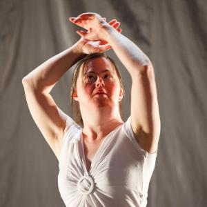 a figure dancing in a white dress with their arms raised above their head