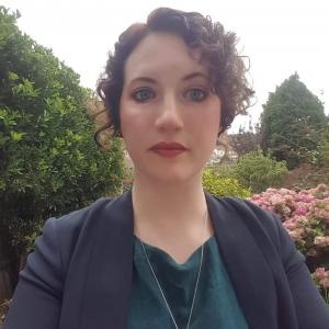 head and shoulder portrait of woman with dark hair in front of a garden