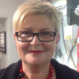 smiling woman with short blond hair black glasses and dark top 