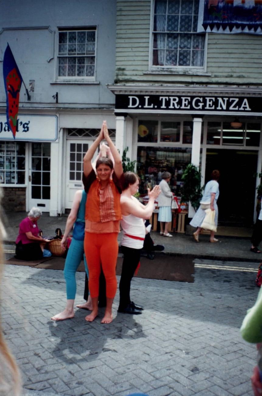A group of people performing in the street at Mazey Day. They are dancing and their is a crowd around them watching. 