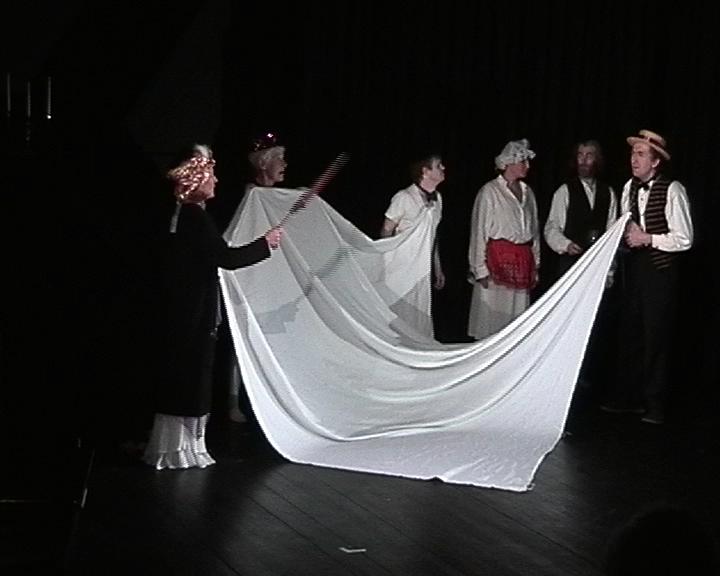 6 people performing on a black stage. They are holding a white sheet together 