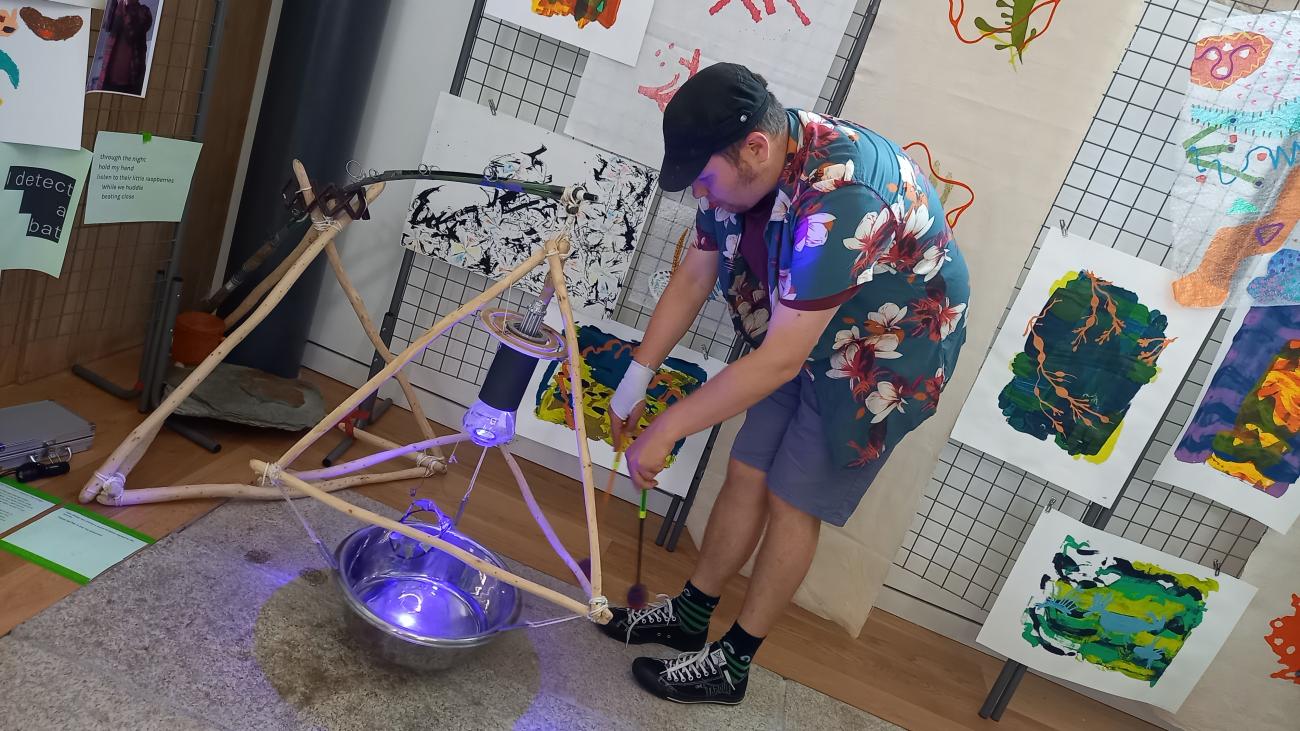 a person playing a homemade instrument which is made out of wood on the floor. The person is bent over hitting it with a stick. 