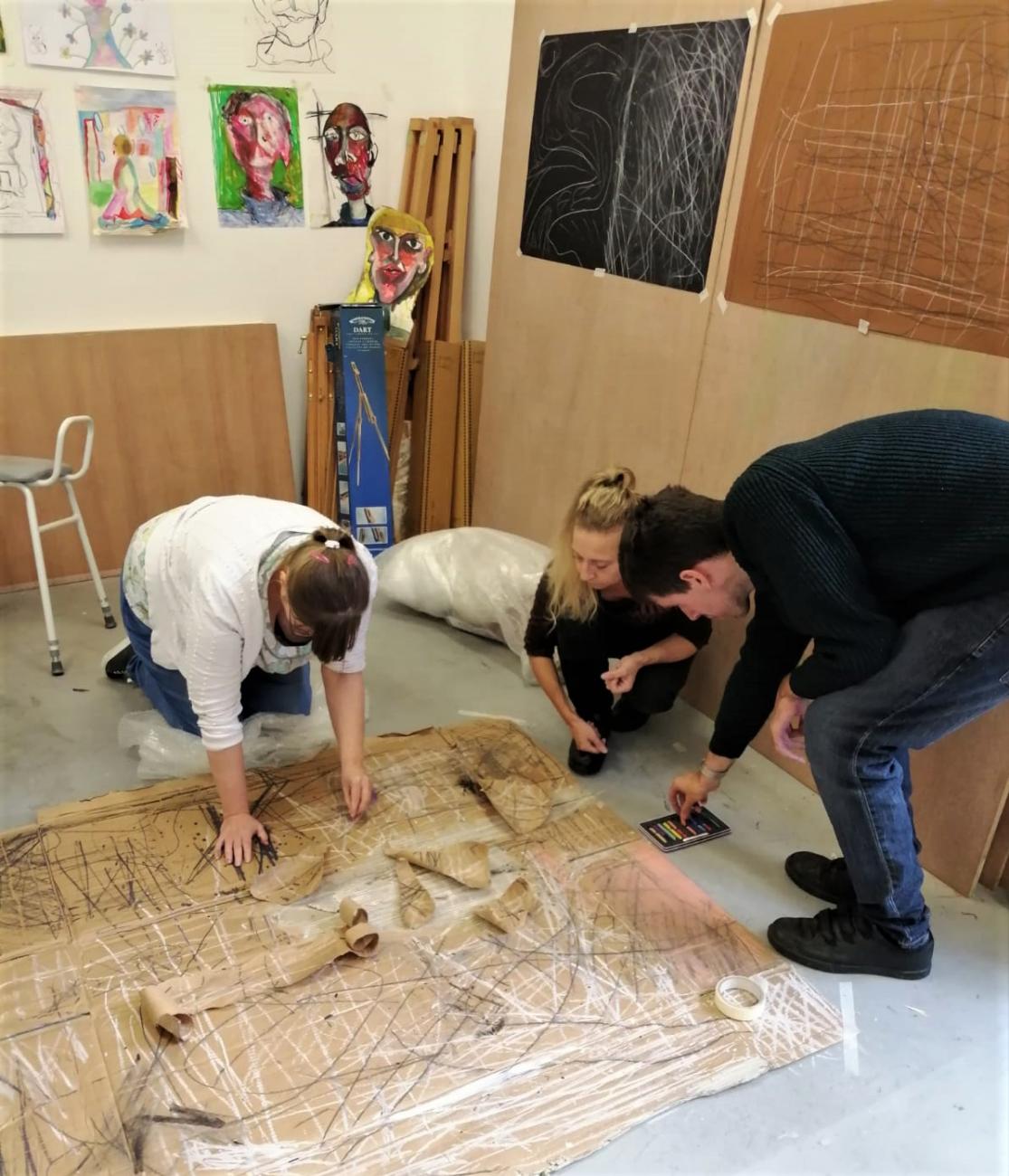 People making art together on the studio floor on large sheets of cardboard