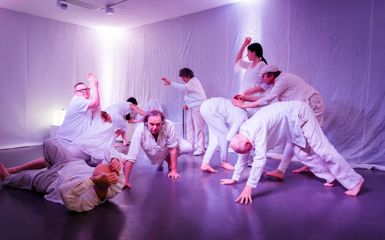 a group of 10 people wearing white dancing in a white gallery space