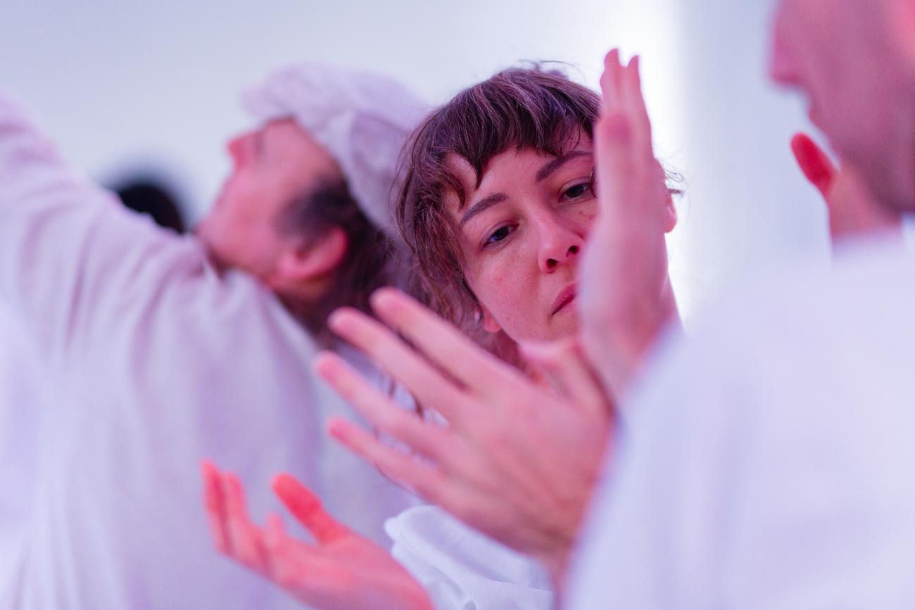 3 people dancing. They are all wearing white. 2 people are spreading their hands out with their wrists together. 