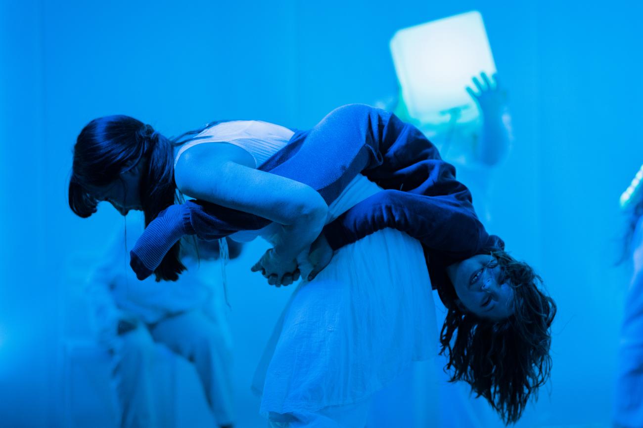 A person carrying a child on their back in a blue room.